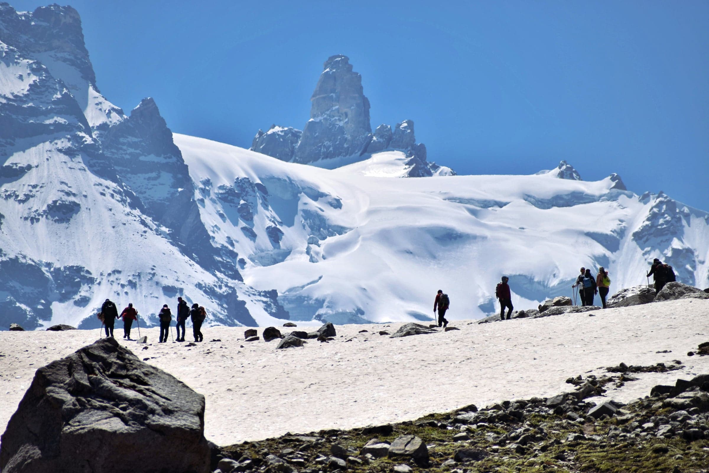 A group of trekkers crossing a snowfield beneath rocky, snow-covered peaks